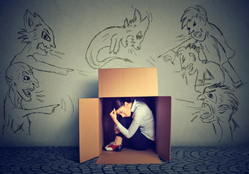 woman hiding in box, sketchings of demons on the wall behind box