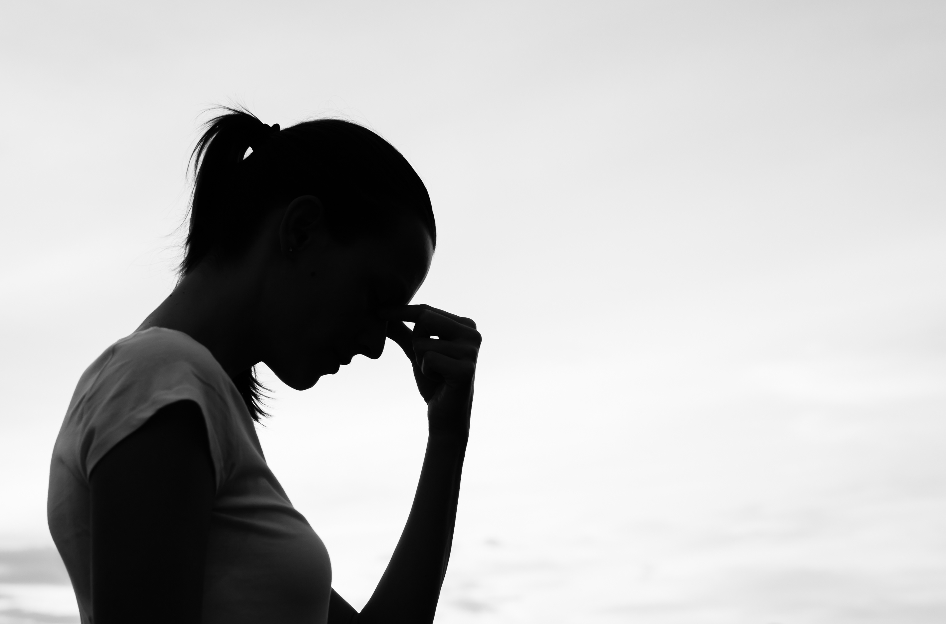 black and white profile of woman holding bridge of nose in pain