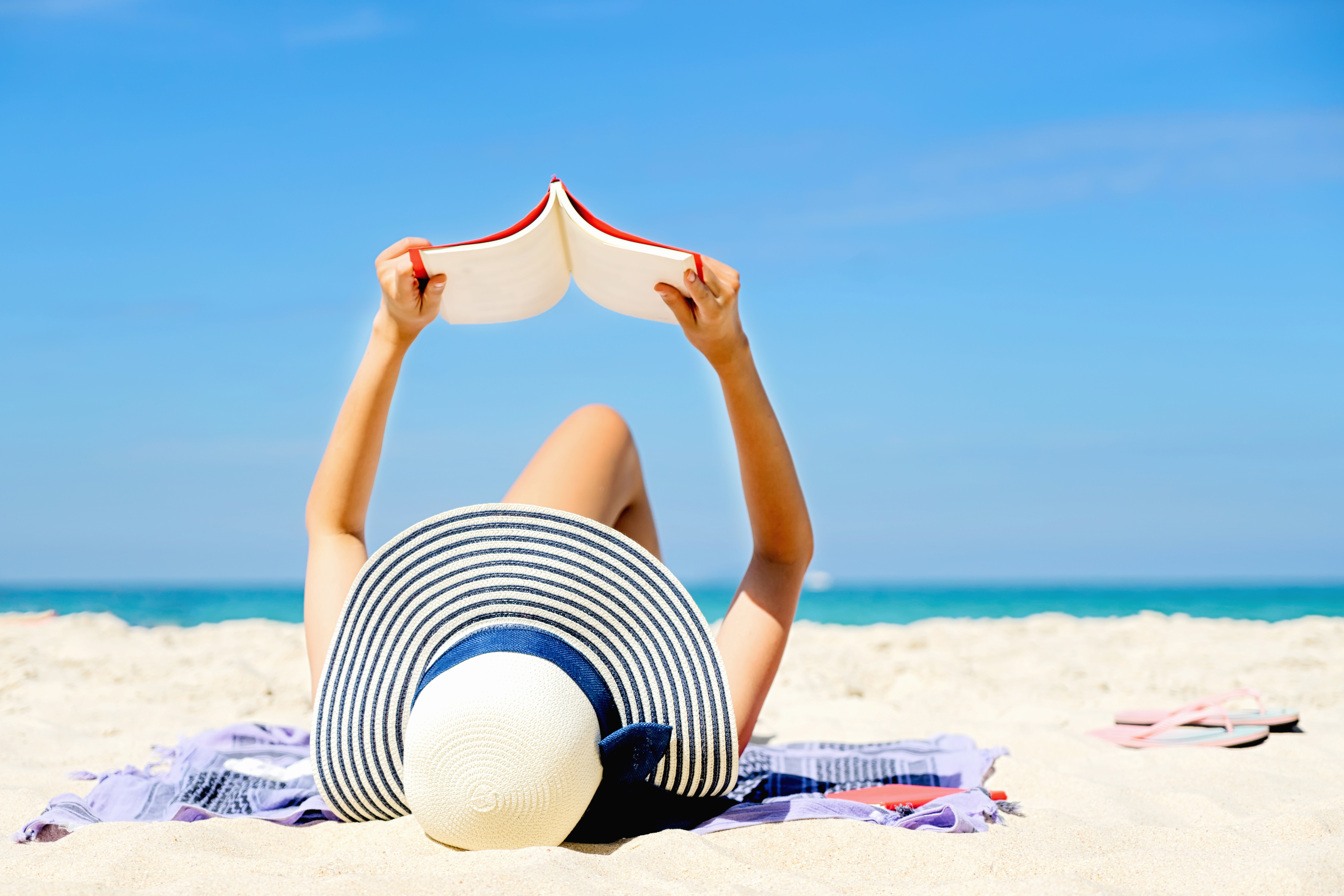 woman in sunhat lying on beach reading a book